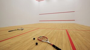 A squash court with wooden flooring, red boundary lines, and two squash rackets. - Hotel Warszawianka (Serock)