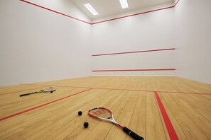 Un court de squash doté d’un plancher en bois, de lignes de démarcation rouges et de deux raquettes de squash.