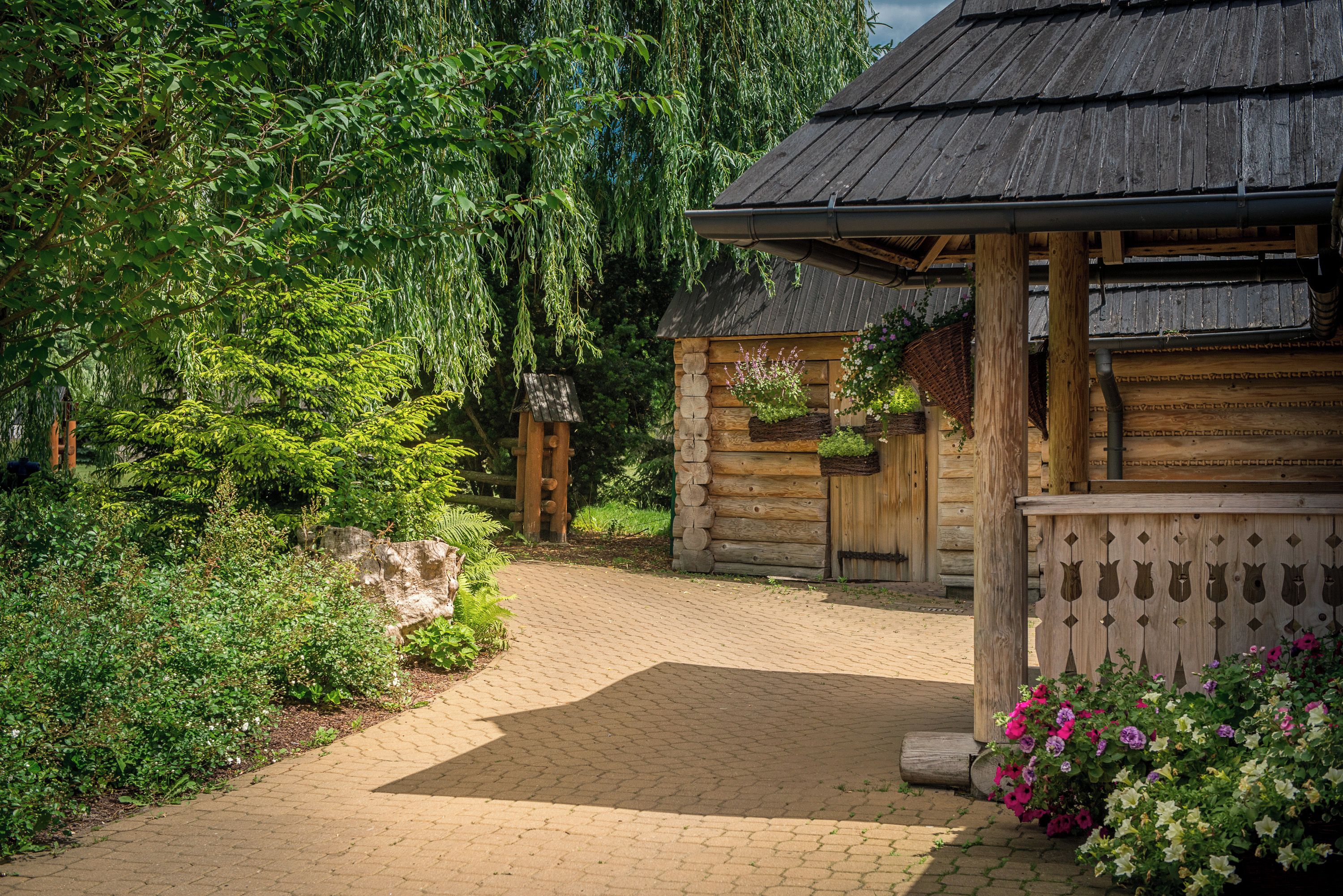 A wooden cabin with a thatched roof, surrounded by lush greenery and a paved pathway.