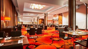 A hotel conference room with multiple tables and chairs, a patterned carpet, and a modern ceiling design. - Hotel Warszawianka (Serock)