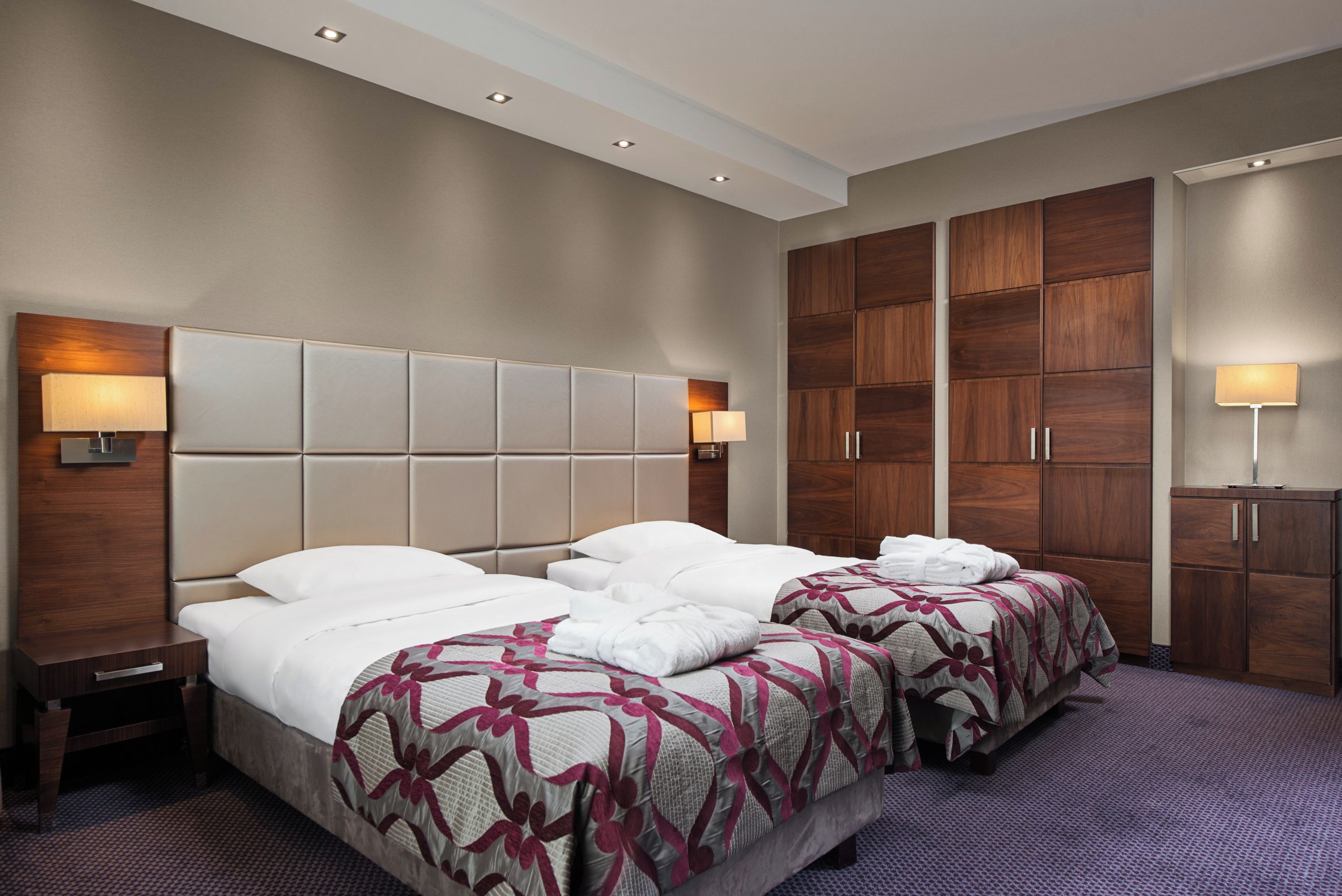 A hotel room with two beds, a large wooden wardrobe, and a small desk.