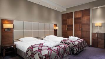 A hotel room with two beds, a large wooden wardrobe, and a small desk.
