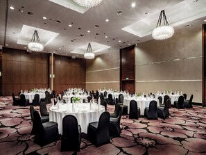 A banquet hall with round tables, black chairs, and chandeliers.