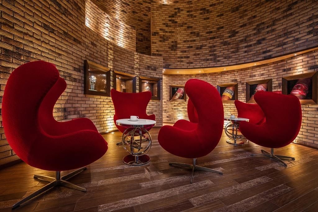 A brick-walled room with red upholstered chairs and a small round table.