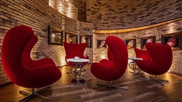 A brick-walled room with red upholstered chairs and a small round table.