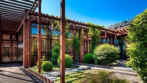 Ein modernes Gebäude mit einer Holzpergola, Glaswänden und einem Garten mit Sträuchern und einem Weg.