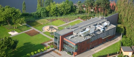A modern building with a flat roof, surrounded by a well-maintained garden and a body of water.