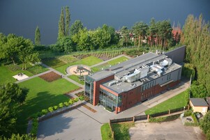 A modern building with a flat roof, surrounded by a well-maintained garden and a body of water.