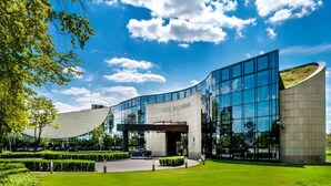 A modern hotel with a curved glass facade, a well-manicured lawn, and a clear blue sky. - Hotel Warszawianka (Serock)