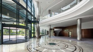 Eine geräumige Lobby mit einem kreisförmigen Mosaikboden, großen Glasfenstern und modernem architektonischem Design.