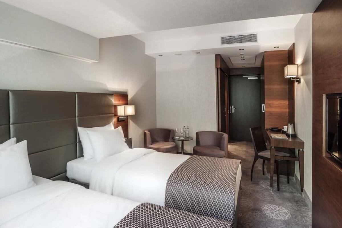 Une chambre d’hôtel avec un grand lit, deux fauteuils, une petite table avec une lampe et un bureau avec une chaise.
