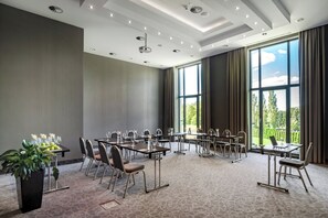 Une salle de conférence dotée de plusieurs tables, de chaises et d’une grande fenêtre donnant sur un paysage verdoyant.