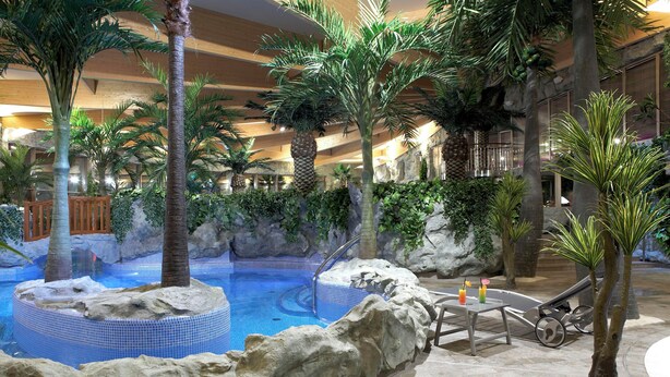 An indoor pool area with a tropical theme, including palm trees and rock formations. - Hotel Warszawianka (Serock)