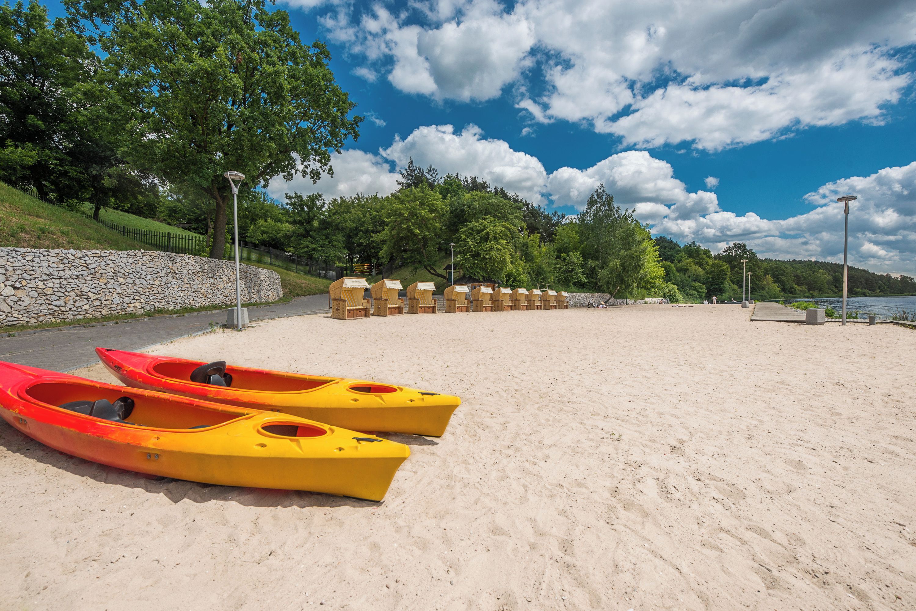 A sandy beach with kayaks and a stone wall.