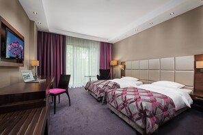 Een hotelkamer met twee bedden, een bureau met een laptop, een stoel en een televisie aan de muur.
