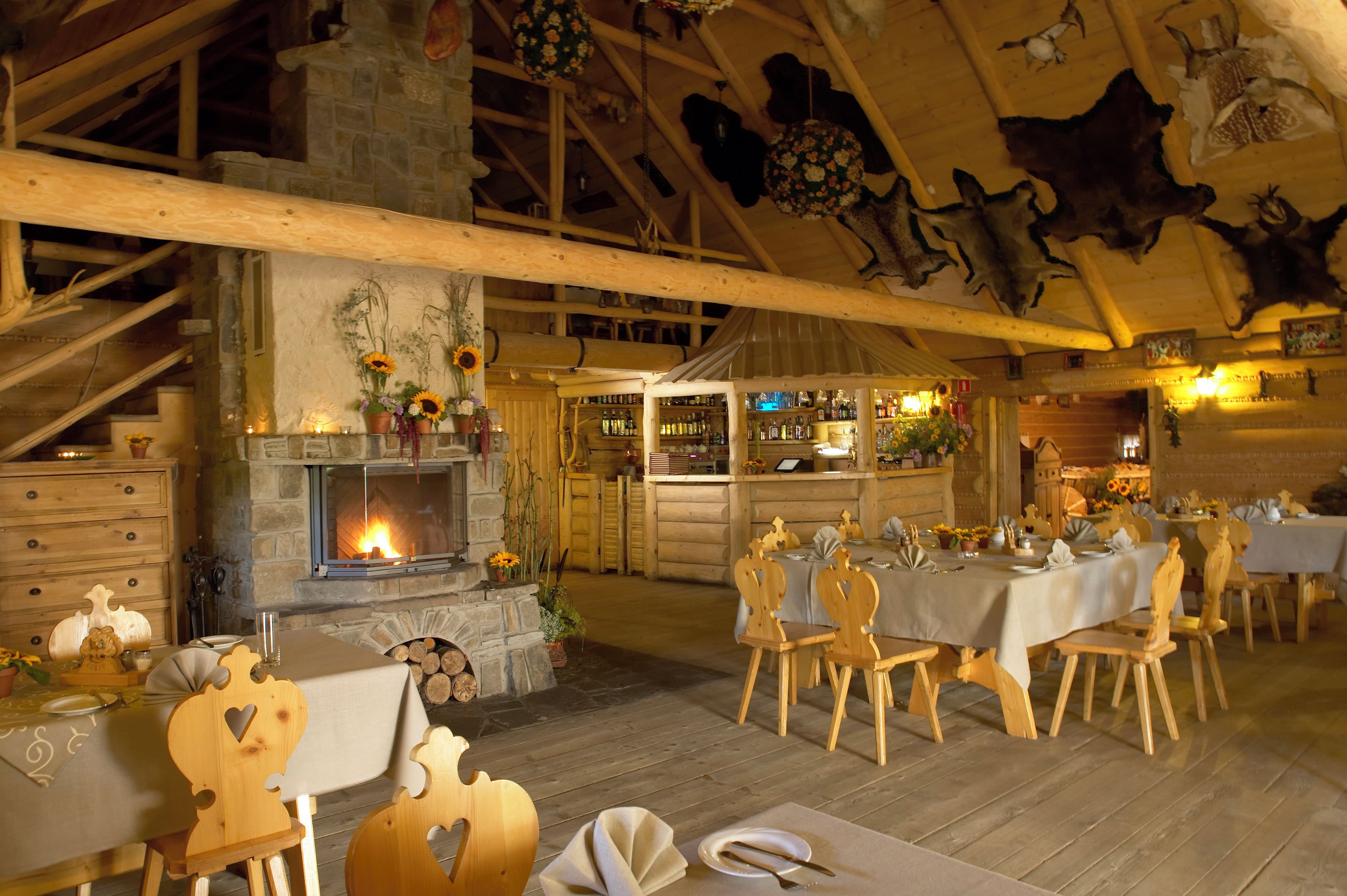 A rustic dining area with wooden furniture, a fireplace, and a bar with shelves of bottles.