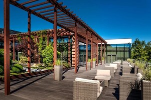 An outdoor patio with wooden pergolas, wicker furniture, and potted plants.