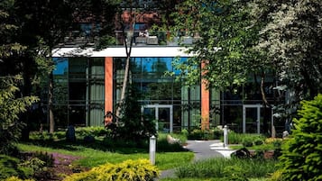 A modern building with a glass facade, surrounded by lush greenery and a pathway leading to the entrance.