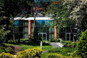 A modern building with a glass facade, surrounded by lush greenery and a pathway leading to the entrance. - Hotel Warszawianka (Serock)