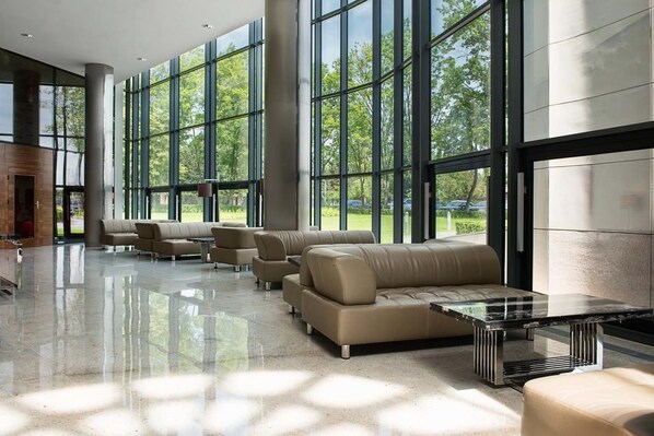 A spacious lobby with large windows, leather sofas, and a glass coffee table. - Hotel Warszawianka (Serock)