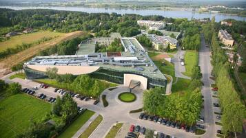 A modern building with a curved roof, surrounded by parking and greenery, overlooking a body of water.