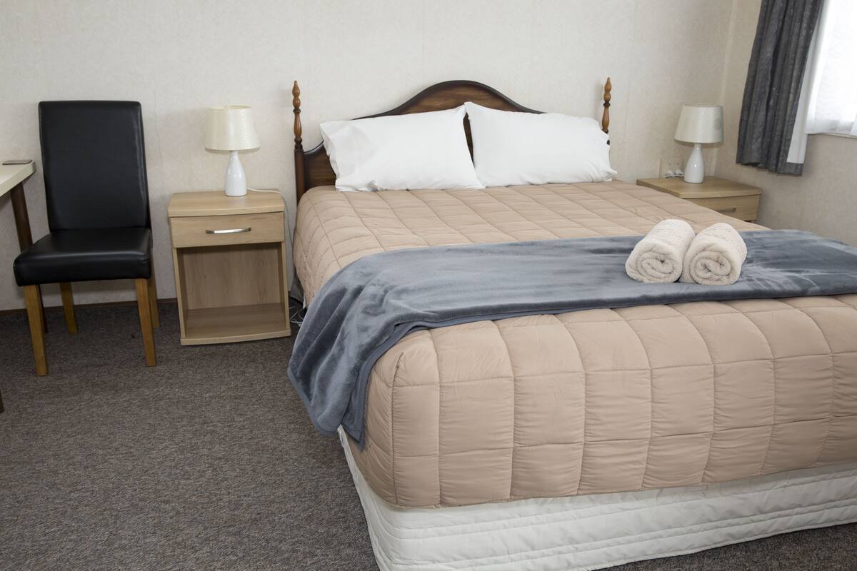 Una habitación de hotel con una cama, una silla, una mesita de noche y una lámpara.