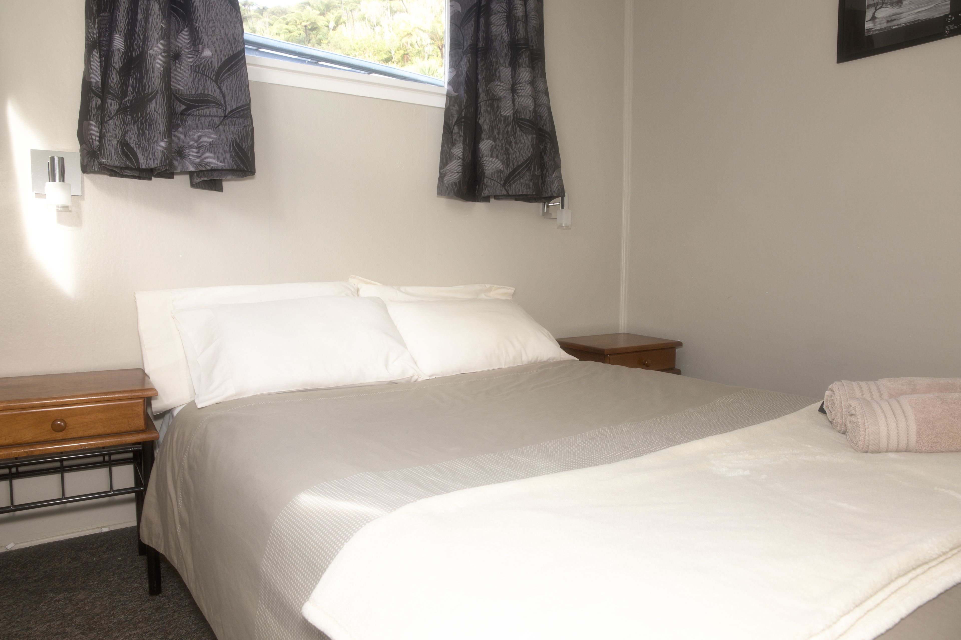 A neatly made bed with white linens, a wooden nightstand, and a window with curtains.