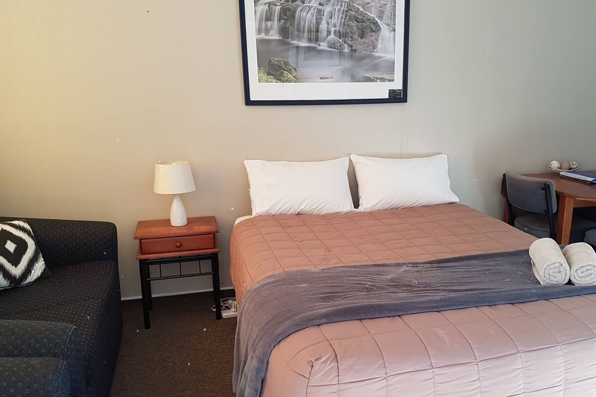 Habitación de hotel con cama, escritorio, silla, microondas y un cuadro en la pared.
