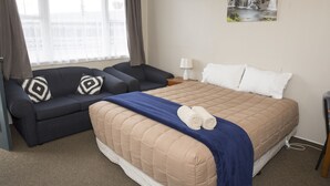 A hotel room with a bed, a sofa, a nightstand, and a window with curtains.