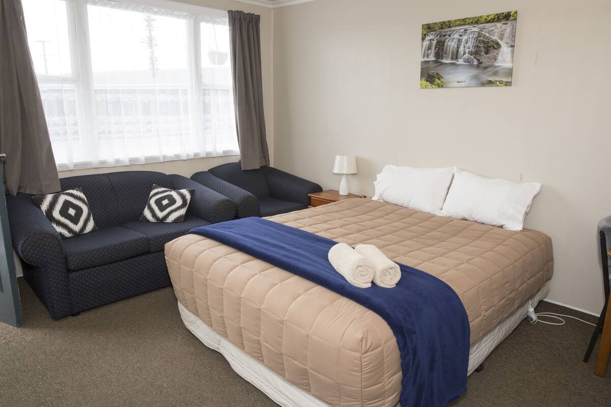 Una habitación de hotel con cama, sofá, mesita de noche y ventana con cortinas.