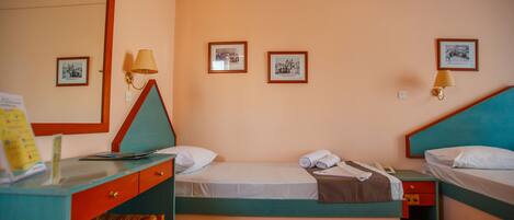 Habitación de hotel con dos camas individuales, un escritorio con silla, un espejo y tres cuadros en la pared.