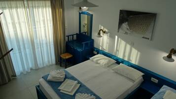 A hotel room with a bed, a desk, a chair, a mirror, and a wall-mounted light fixture.