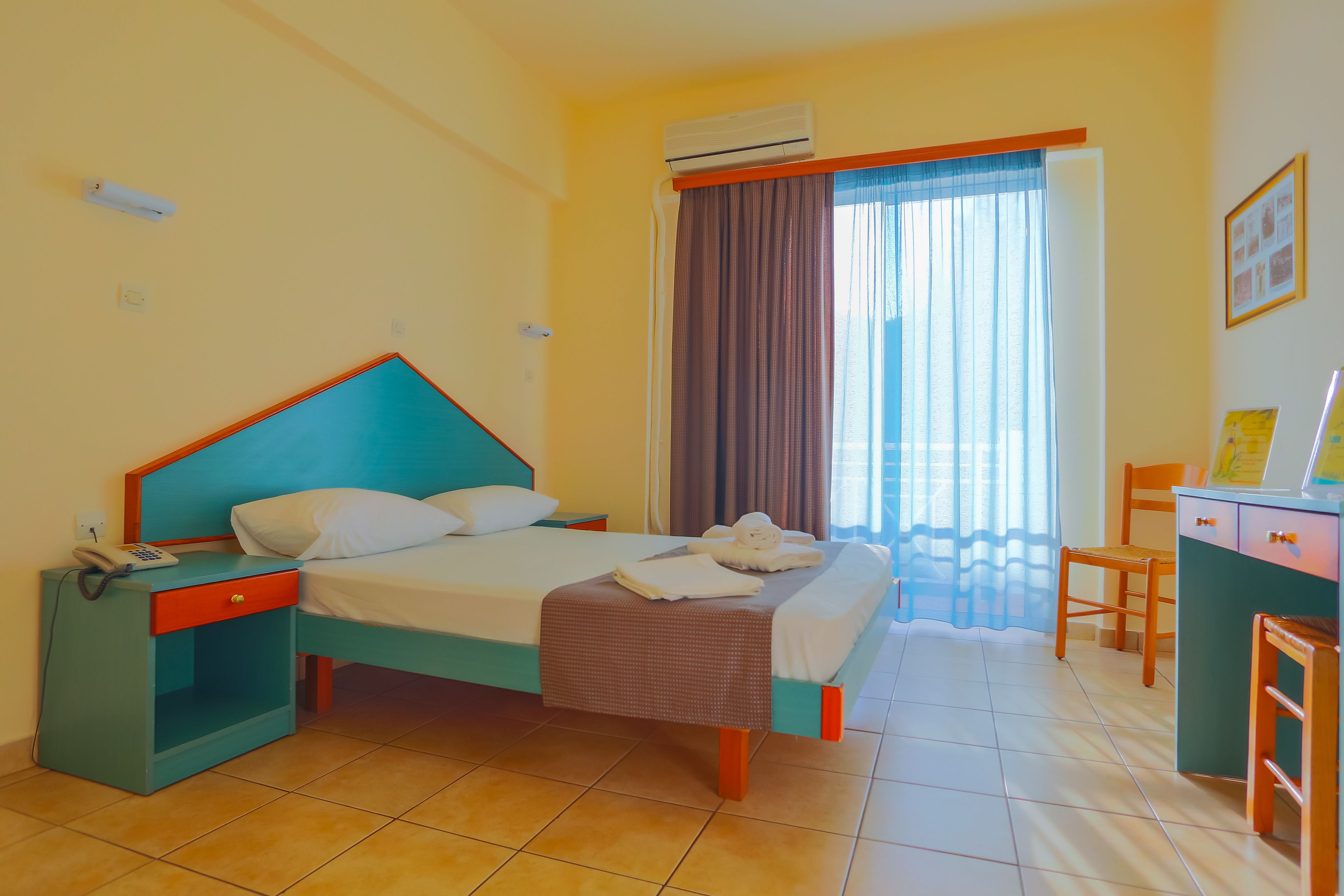 A hotel room with a bed, a desk, a chair, a telephone, and an air conditioning unit.