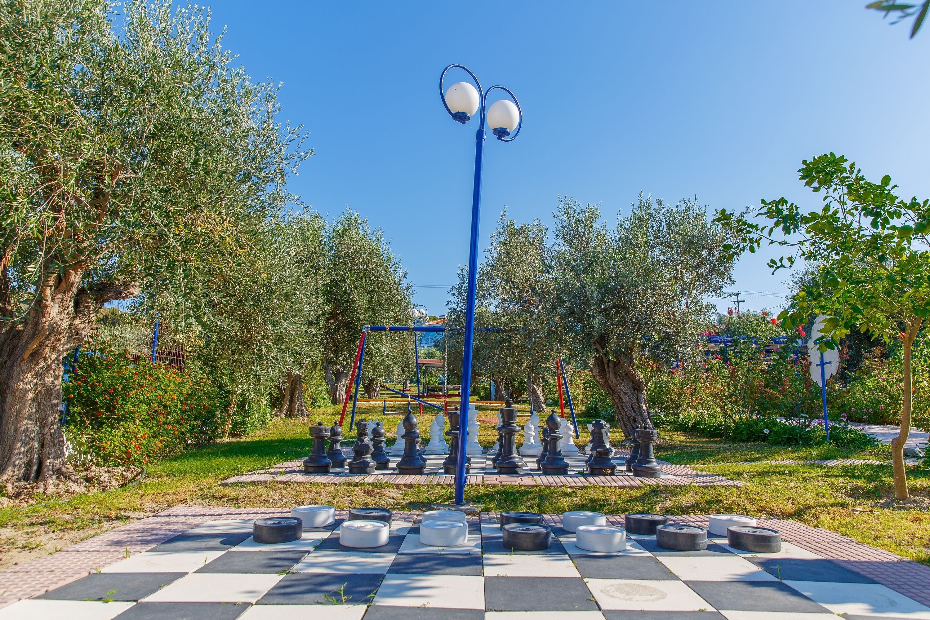 A park with a chessboard, trees, and a street lamp.