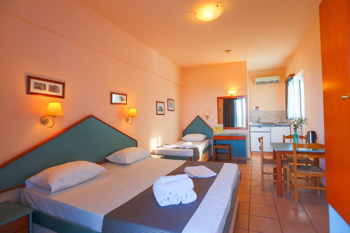 A hotel room with two beds, a desk, and a kitchenette.