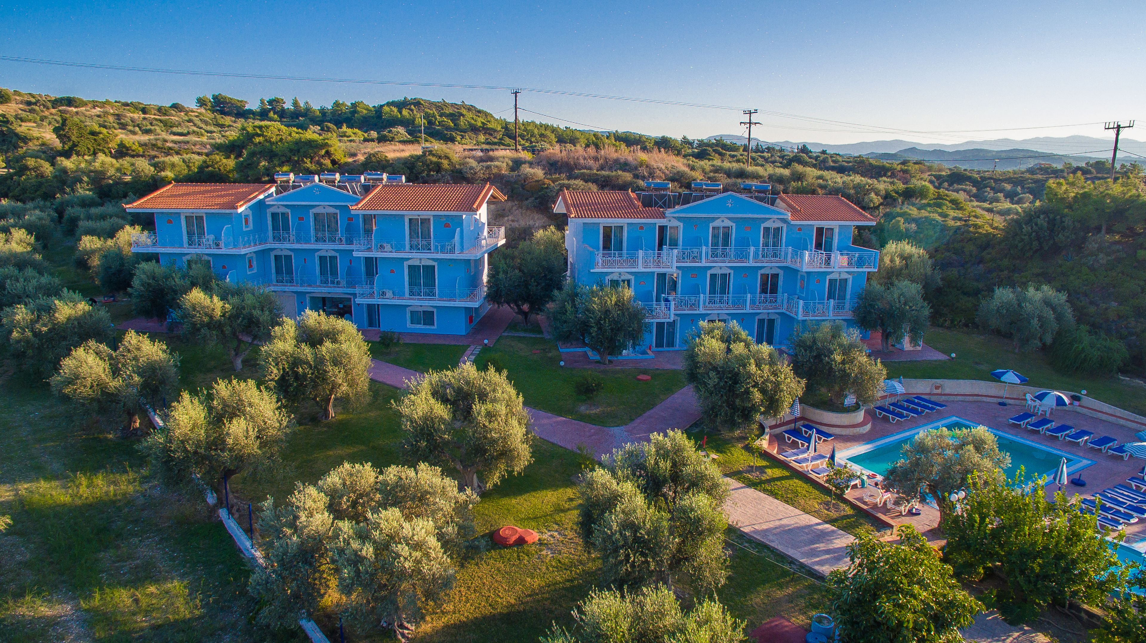 A large blue building with multiple balconies, surrounded by trees and a swimming pool.