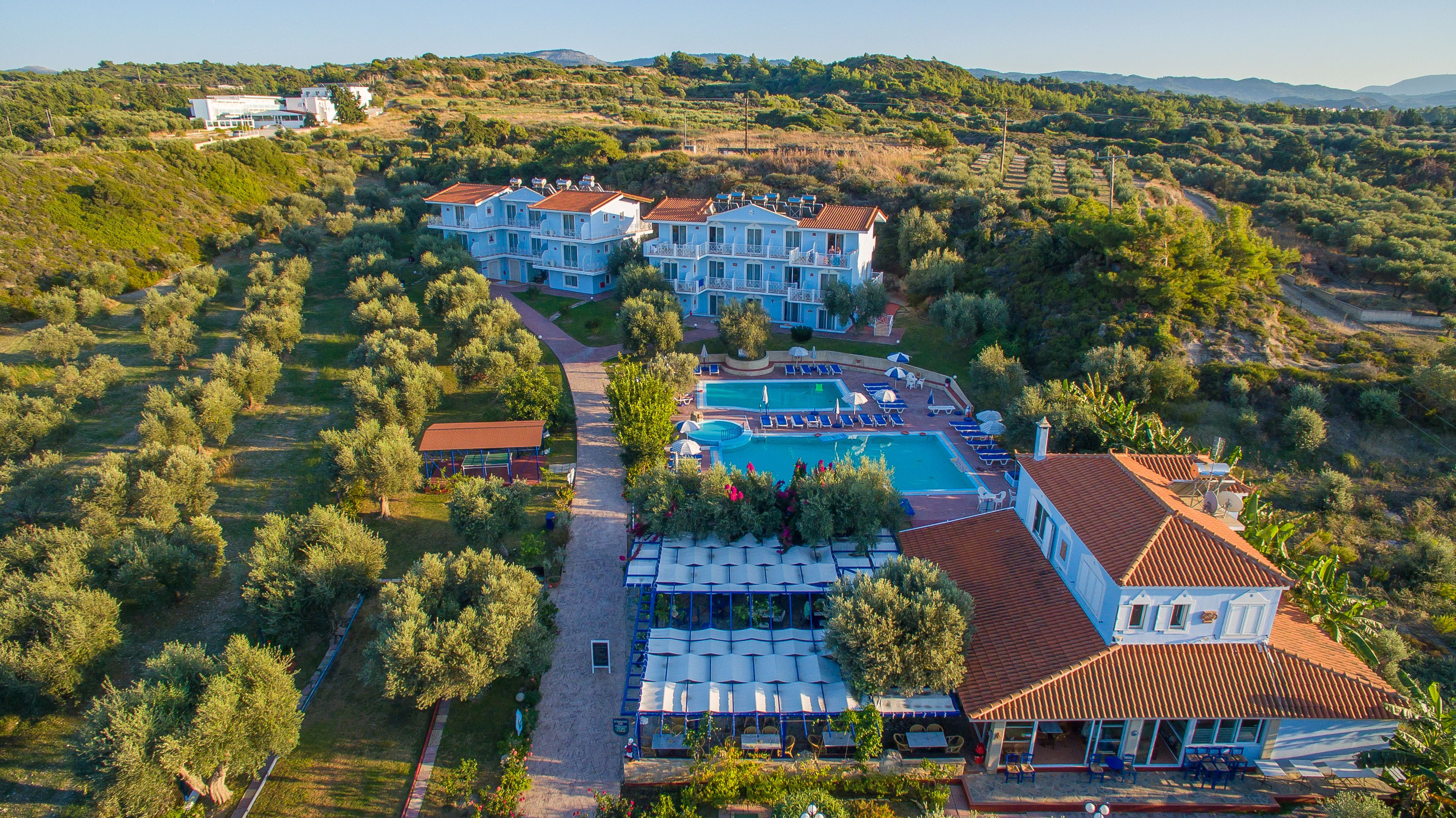 A large resort with multiple buildings, a swimming pool, and lush greenery.
