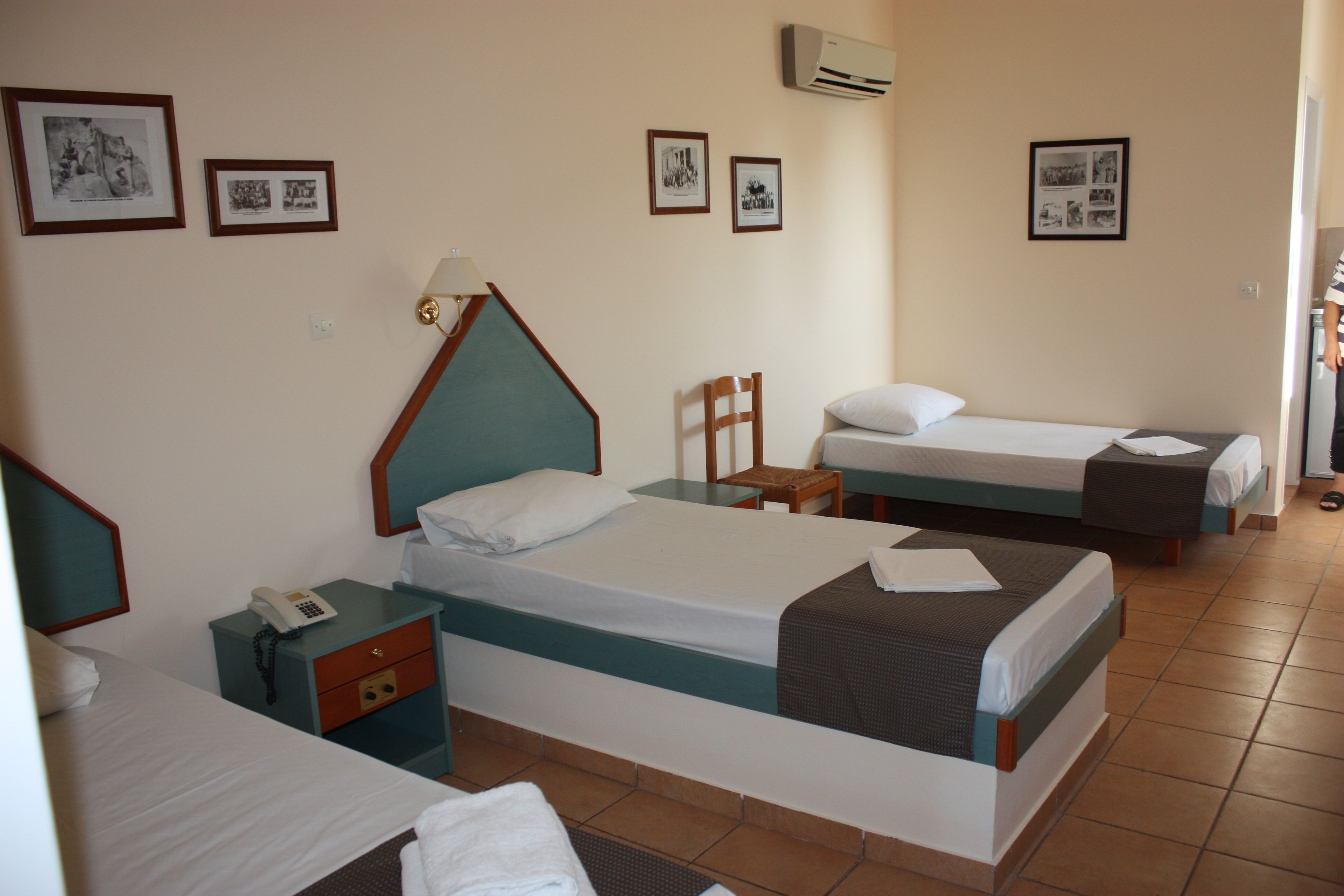 A hotel room with three beds, a desk with a telephone, and a chair.