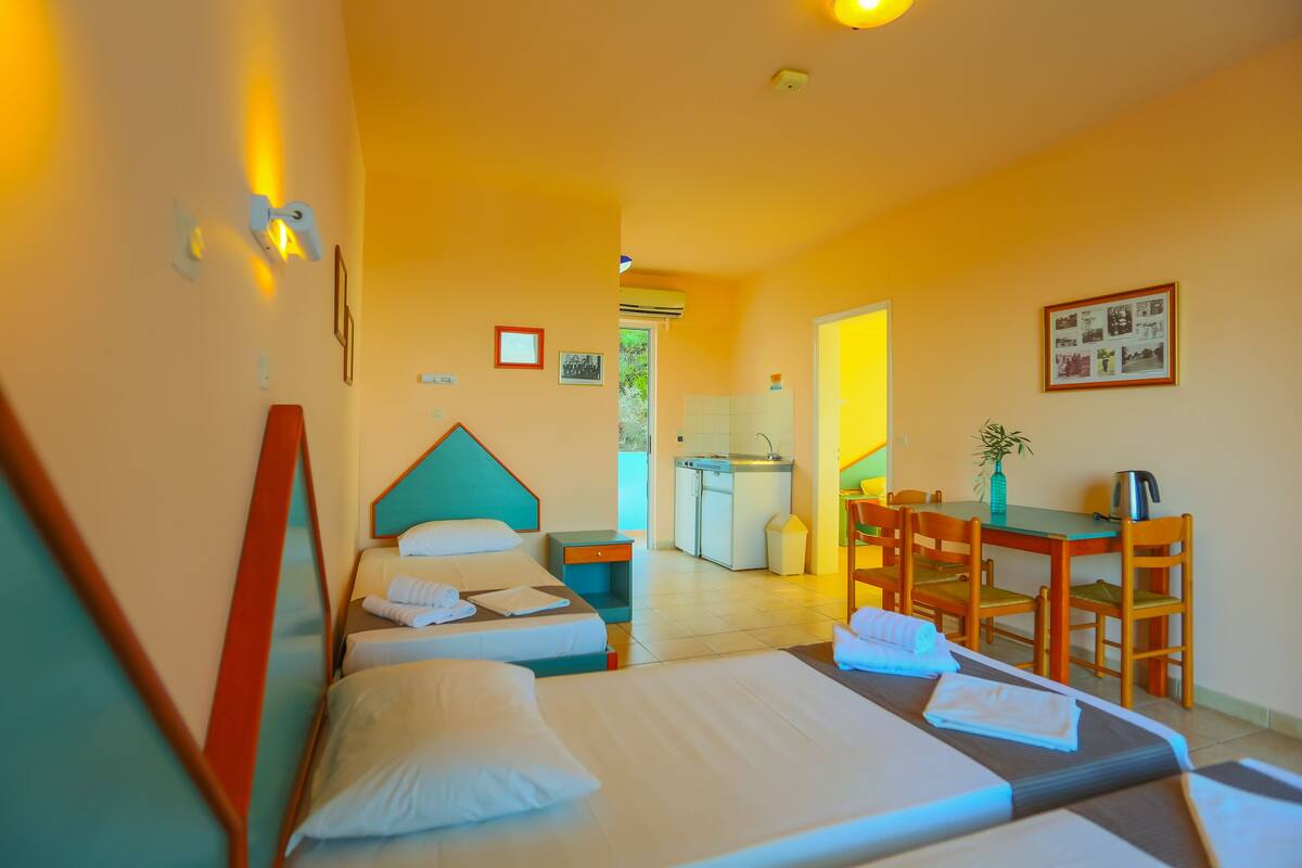 A hotel room with two beds, a kitchenette, a dining area, and a bathroom.