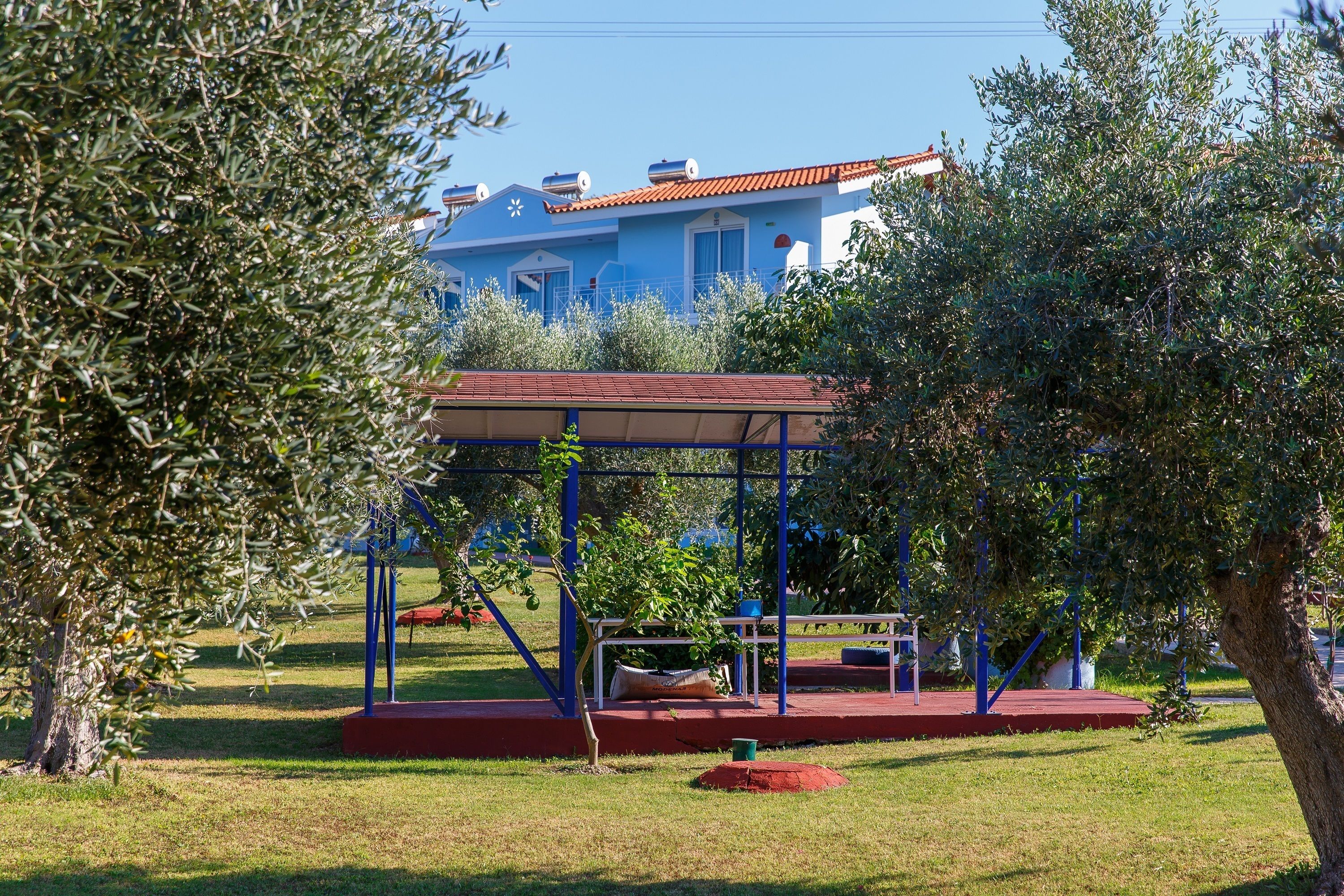 A blue house with a red roof, surrounded by trees and a swing set.