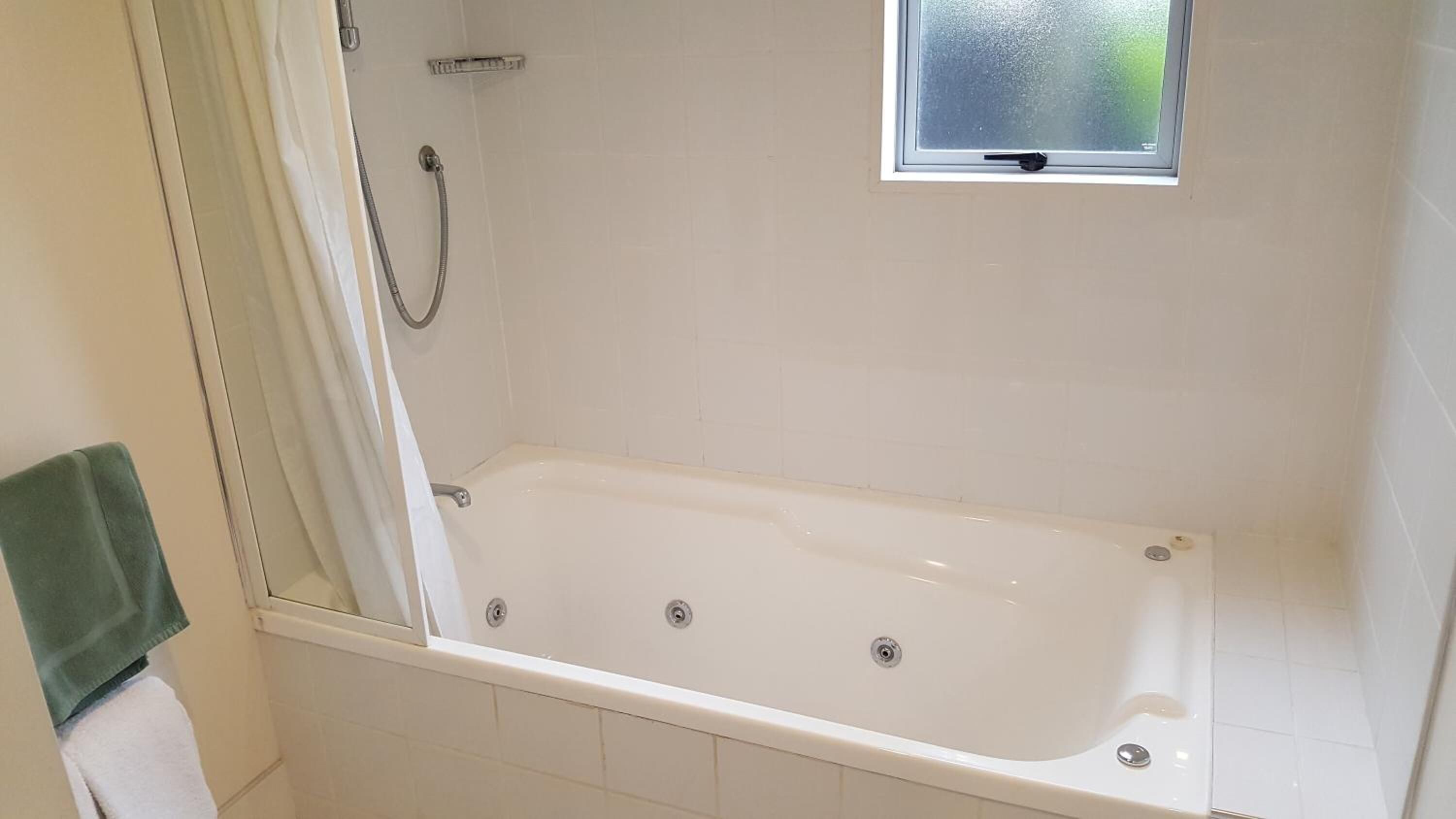 A bathroom with a bathtub, a shower, and a small window.