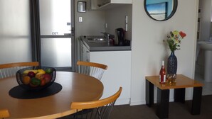 A modern kitchen with a sink, a coffee maker, and a fruit bowl on the table. There is a mirror on the wall and a vase with flowers on a side table. - Fyffe On Riccarton (Christchurch)
