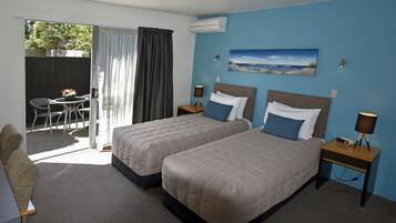 Habitación de hotel con dos camas, un escritorio y una silla. Hay un cuadro en la pared y un equipo de aire acondicionado sobre la cama.