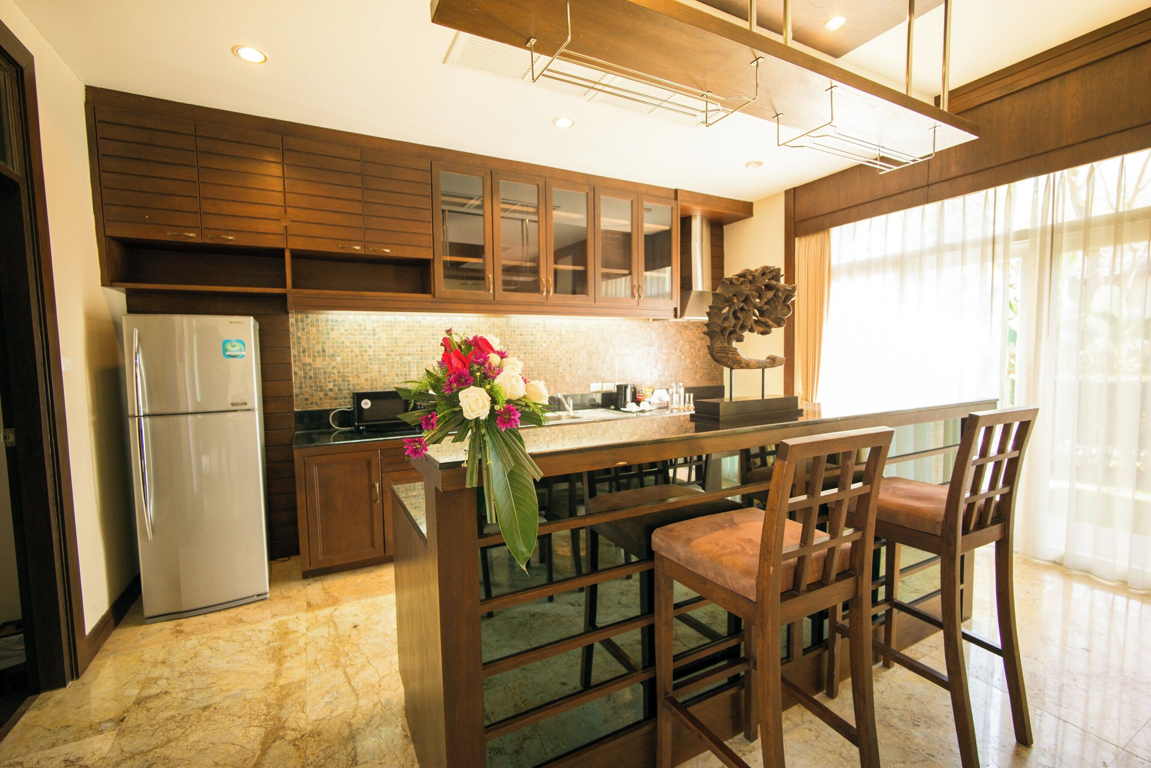 A modern kitchen with wooden cabinets, a marble countertop, and a built-in island with bar stools.