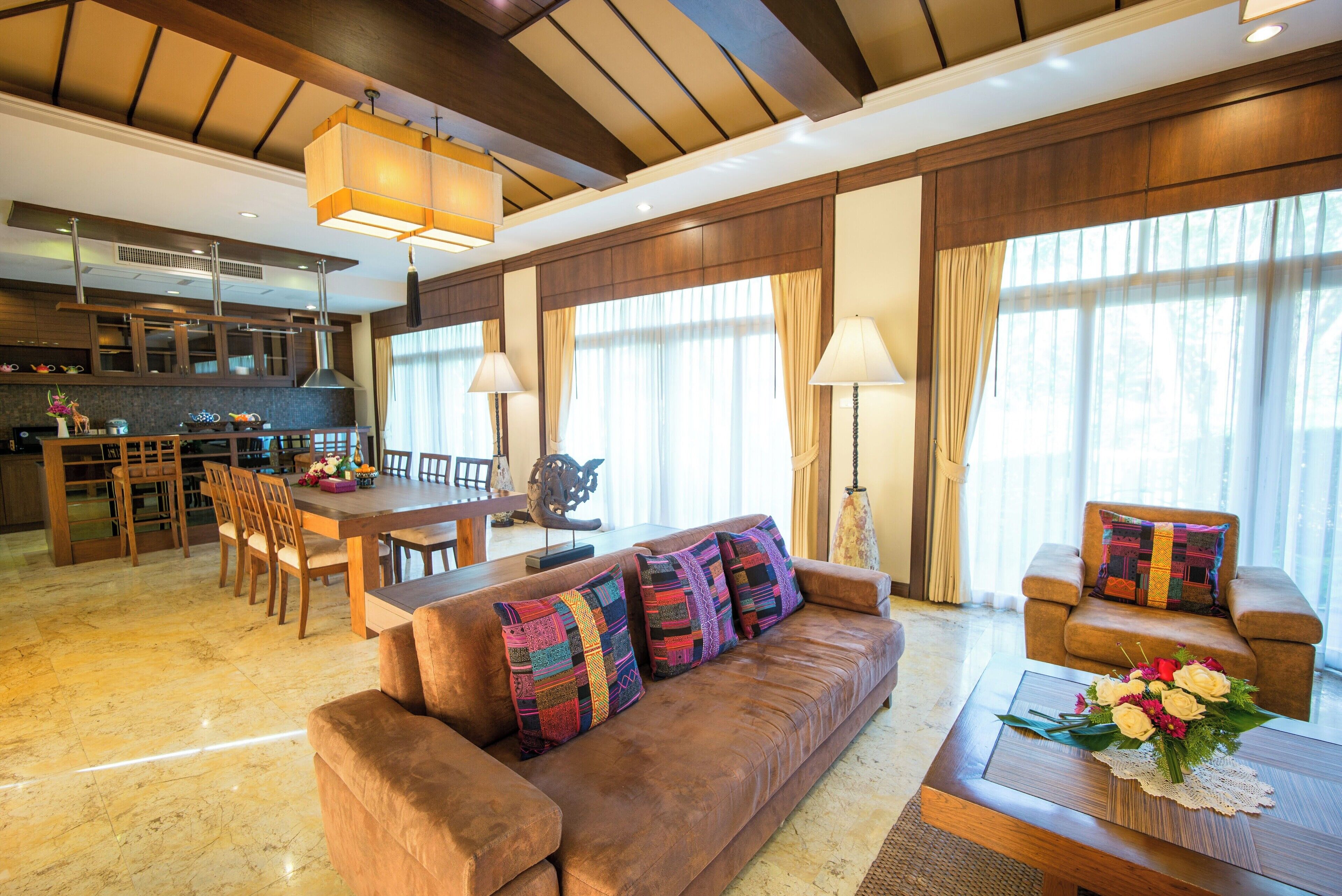 A spacious living area with a brown sofa, a dining table, and a kitchen in the background.