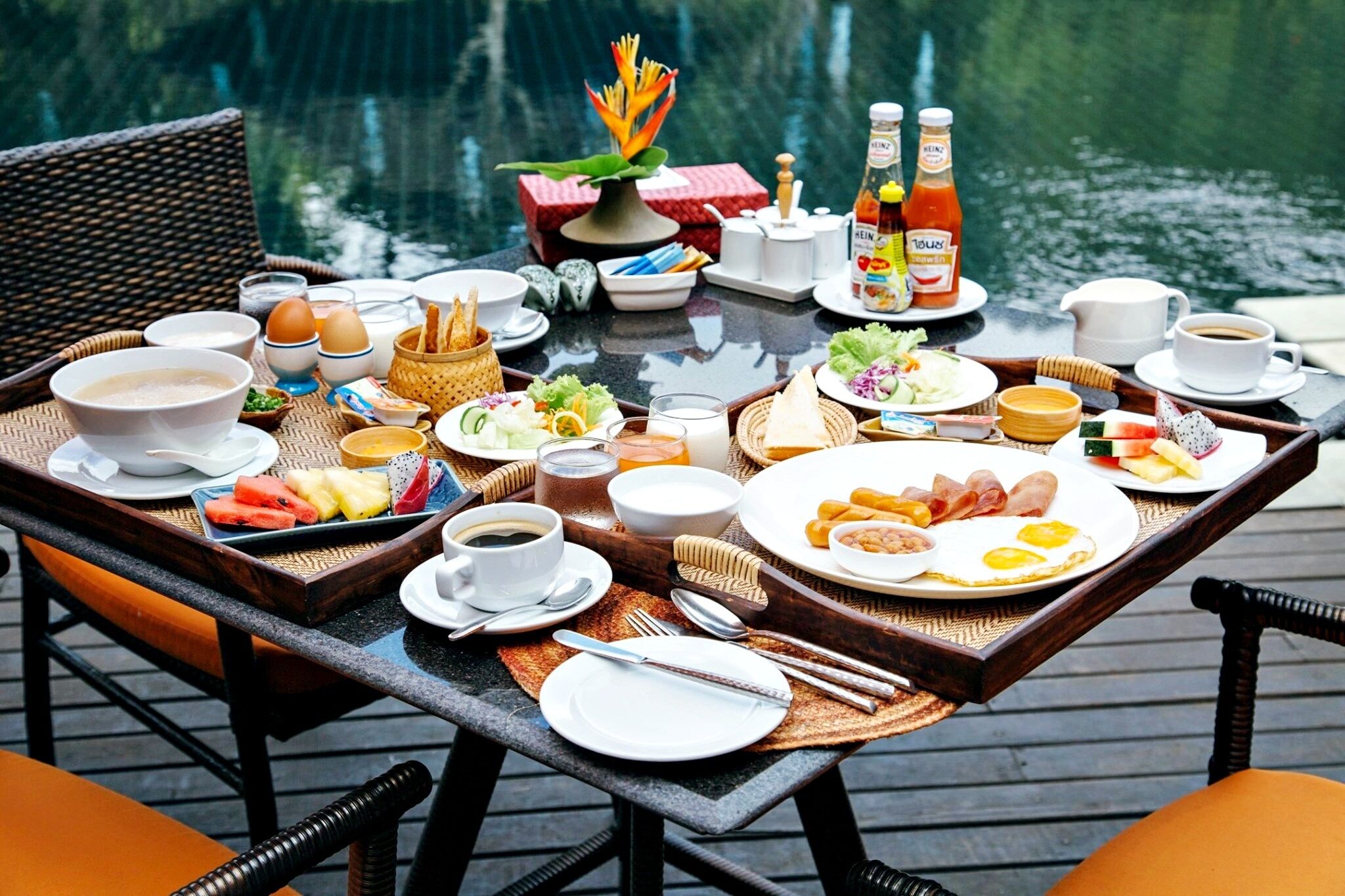 A breakfast table set on a wooden deck with a view of a body of water.
