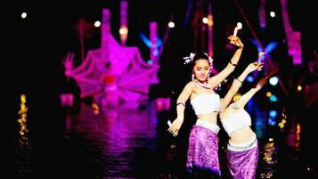 A person in a white top and purple skirt performing on a stage with a large pink structure in the background.