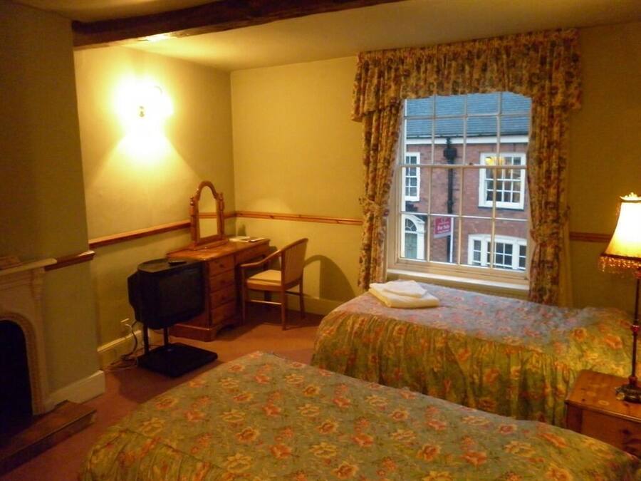 Une chambre d’hôtel avec deux lits, un bureau avec une chaise, une télévision, une cheminée et une fenêtre avec des rideaux.