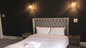 A bedroom with a tufted headboard, white bedding, two bedside tables, and a remote control on one of the tables. - Dixie Arms (Nuneaton)