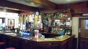 A bar area with a wooden counter, stools, and shelves stocked with bottles. - Dixie Arms (Nuneaton)